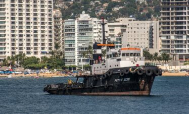 A tugboat sailing in Acapulco with a backdrop of skyscrapers and beach.
