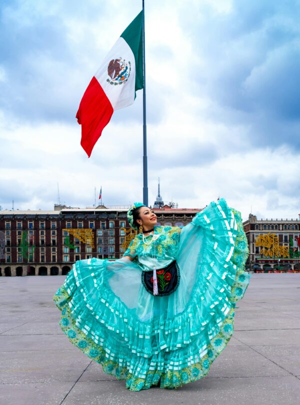 Colorful Mexican dancer twirls in a traditional dress with national flag in the background.