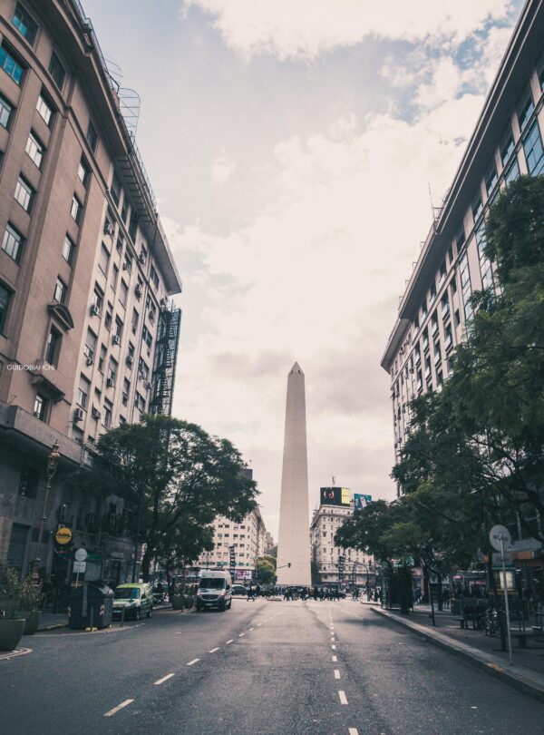 The iconic Obelisk of Buenos Aires towers between tall buildings on Avenida Corrientes.