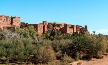 Explore the ancient architecture of Ait Benhaddou Kasbah set against Morocco's lush desert landscape.