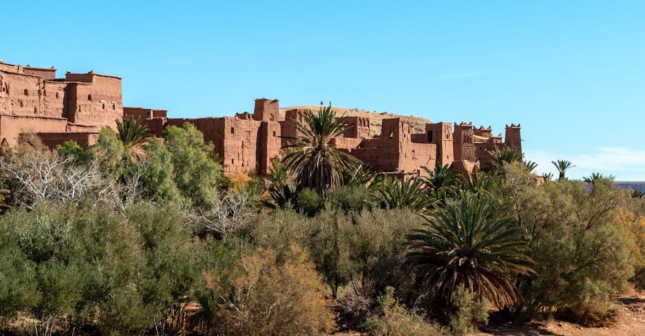 Explore the ancient architecture of Ait Benhaddou Kasbah set against Morocco's lush desert landscape.