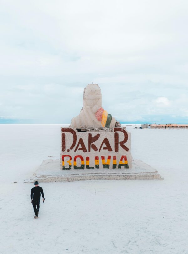 A solitary traveler approaches the Dakar Rally Monument in the vast Salar de Uyuni, Bolivia.