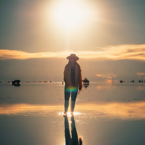 A person stands silhouetted against a glowing sunset on the reflective surface of Salar de Uyuni, Bolivia.