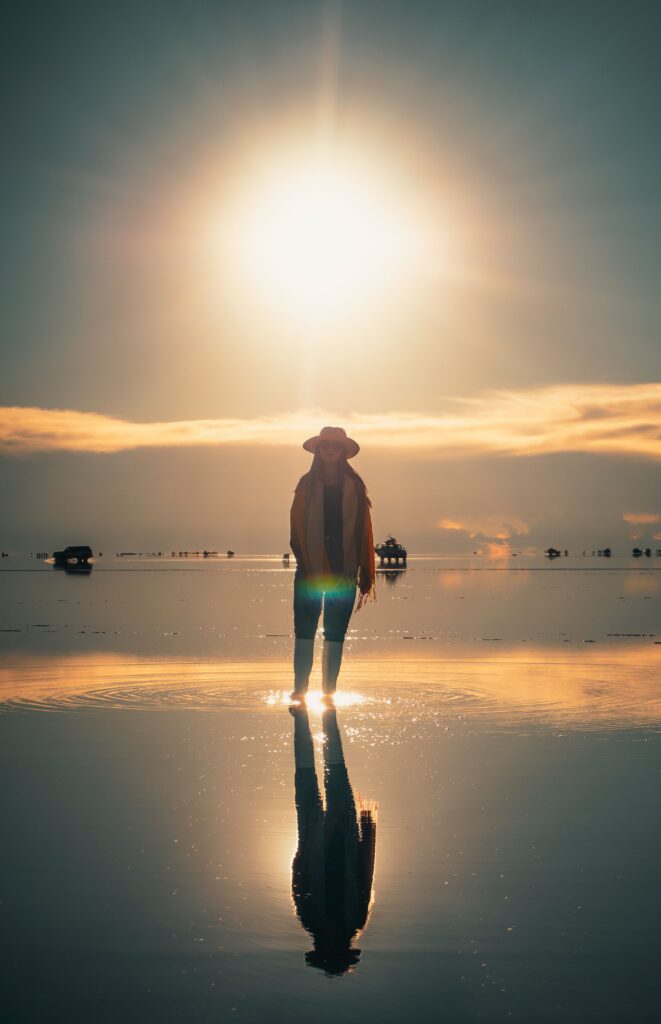 A person stands silhouetted against a glowing sunset on the reflective surface of Salar de Uyuni, Bolivia.