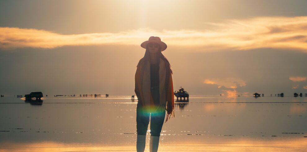 A person stands silhouetted against a glowing sunset on the reflective surface of Salar de Uyuni, Bolivia.